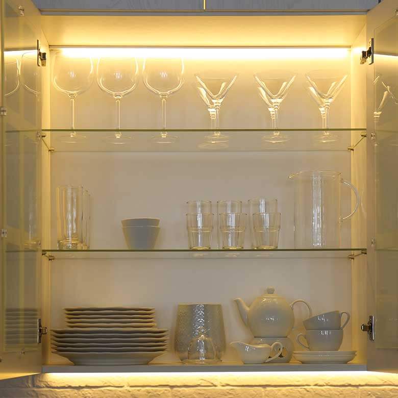 glass shelving lit up on top and bottom with drinking glasses on shelves